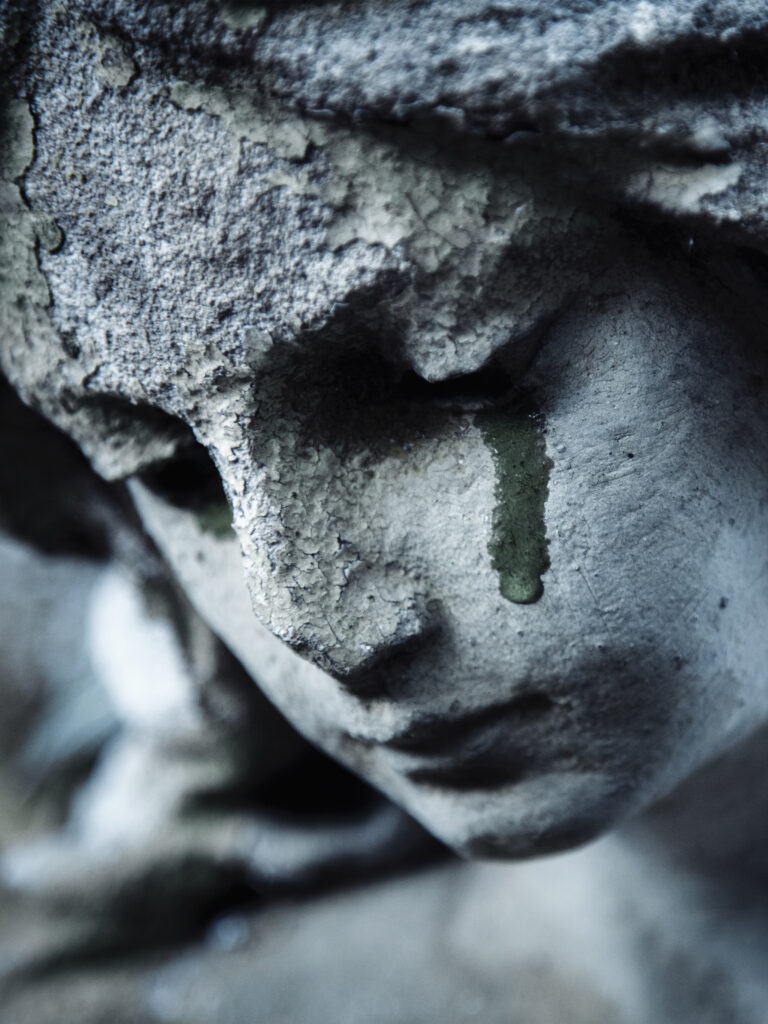 Ancient stone statue of crying sad angel with tears in face as symbol of death and end of human life.
