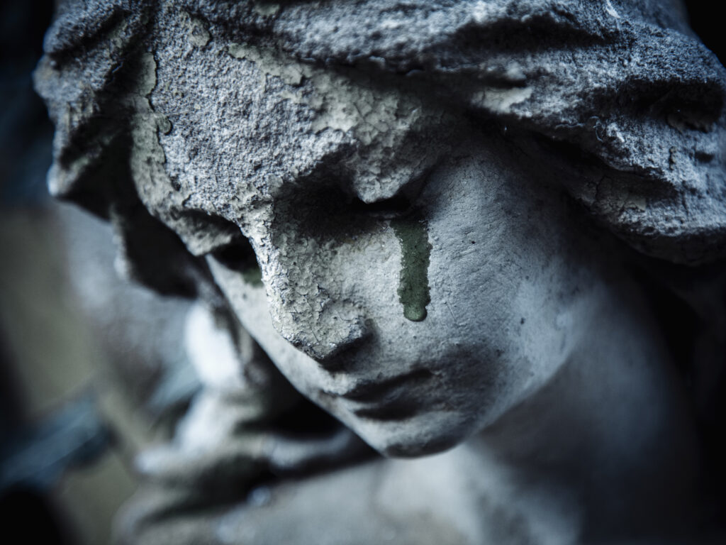 Ancient stone statue of crying sad angel with tears in face as symbol of death and end of human life.